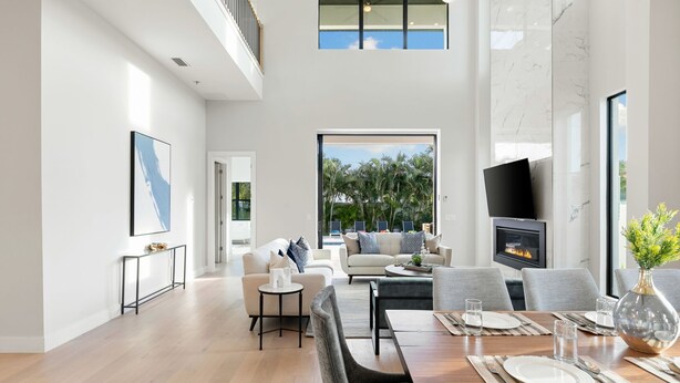 A spacious living area with a high ceiling, a fireplace, a dining table set for four, and a large window overlooking greenery. - 560 Perfectly Situated · Walk 2 Beaches & The Ritz (Naples)