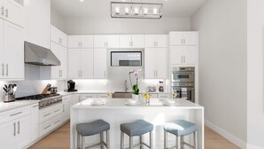 A modern kitchen with white cabinetry, a central island with stools, a stove, and a large window. - 560 Perfectly Situated · Walk 2 Beaches & The Ritz (Naples)