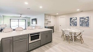 Une cuisine moderne avec des meubles gris, un grand îlot central et un coin repas doté de chaises en osier.
