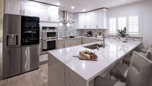Una cocina moderna con armarios blancos, electrodomésticos de acero inoxidable, una isla de mármol y horno empotrado.