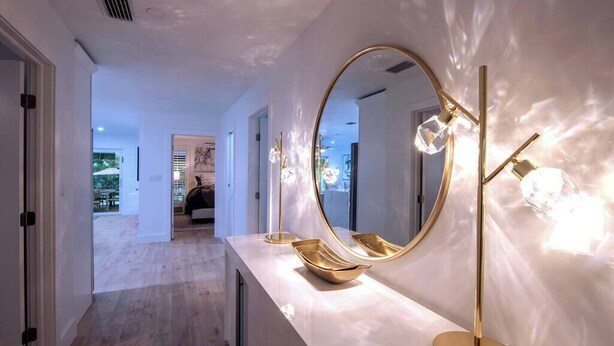 Un baño moderno con un espejo grande, una lámpara de pie dorada y un tocador blanco.