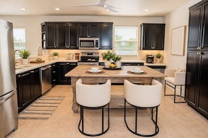 A modern kitchen with dark cabinetry, a central island with chairs, a microwave, oven, and a refrigerator. - 10082 Paradise Palms Retreat (Naples)