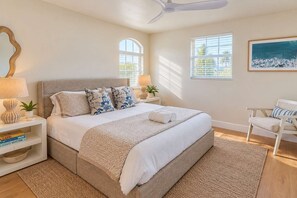 A bedroom with a large bed, bedside tables, a chair, a ceiling fan, and a window.