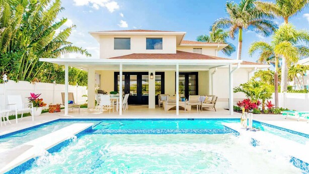 Ein zweistöckiges Haus mit überdachter Terrasse, Schwimmbad und tropischer Bepflanzung.