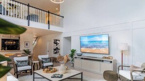 Ein geräumiges Wohnzimmer mit großem Fernseher, bequemen Sitzmöglichkeiten, einer Treppe und Blick ins Freie.