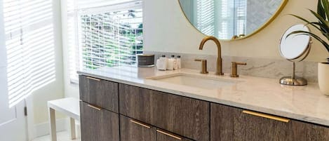 Un baño moderno con un tocador grande, un espejo redondo y una lámpara sobre el espejo.