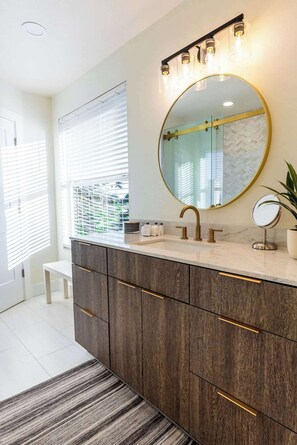 A modern bathroom with a large vanity, a round mirror, and a light fixture above the mirror.
