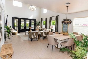 A spacious dining area with a large table and chairs, surrounded by windows and potted plants.