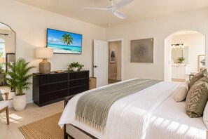 A bedroom with a bed, a dresser, a ceiling fan, a painting, and a door leading to another room. - 10082 Paradise Palms Retreat (Naples)