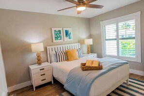 A bedroom with a bed, two bedside tables, a ceiling fan, artwork on the wall, and a window with blinds. - 5331 Aqua Haven - Waterfall Pool (Naples)