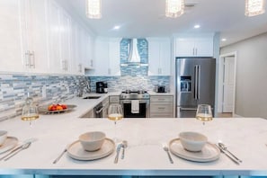 A modern kitchen with white cabinets, a stainless steel refrigerator, and a tiled backsplash. - 5332 Aqua Haven - Waterfall Pool (Naples)