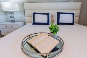 A neatly made bed with a headboard, a bedside table with a lamp, and a tray with a book and a small plant. - 5332 Aqua Haven - Waterfall Pool (Naples)