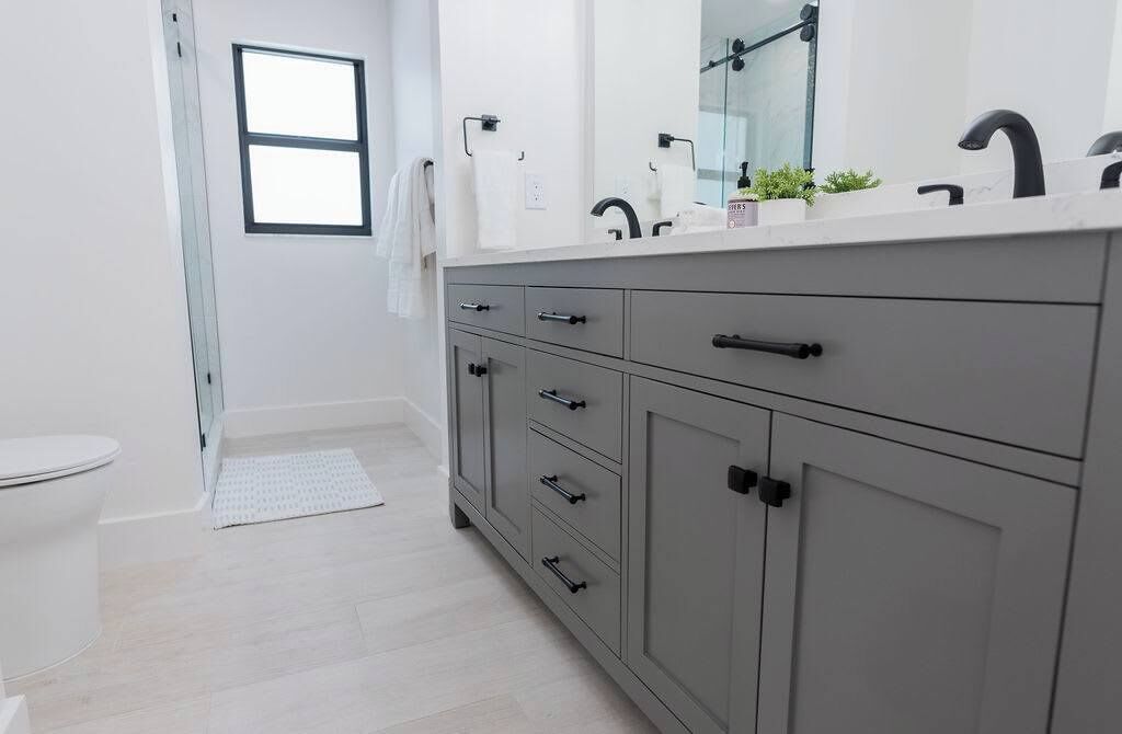 A modern bathroom with a white sink, dark gray cabinets, and a white toilet.
