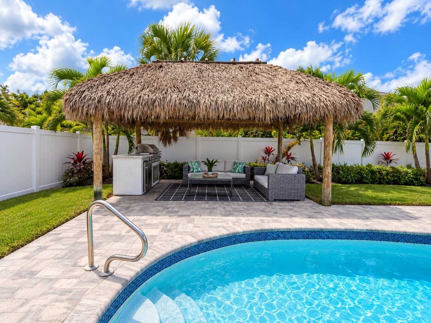 A poolside area with a thatched roof structure, outdoor seating, and a swimming pool.