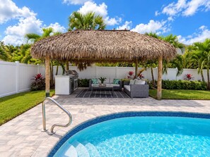 A poolside area with a thatched roof structure, outdoor seating, and a swimming pool.