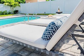 A poolside area with lounge chairs, a pool, and a small fountain. - 538 Chic Tiki Cottage · Saltwater Pool· Walk2Beach (Naples)