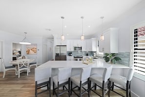 A modern kitchen with white cabinetry, a central island with bar stools, pendant lighting, and a view of the dining area.