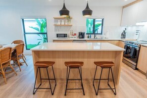 Una cocina moderna con una isla central, taburetes de bar, microondas, cafetera y estufa.