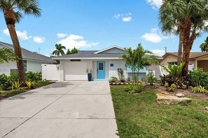 A single-story house with a blue door, surrounded by palm trees and a well-maintained lawn.