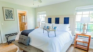 A bedroom with a bed, bedside tables, a bench, and a door leading to another room. - 798 Barefoot Bungalow ·Heated Pool/Spa· Bike2Beach (Naples)