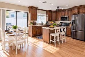 A modern kitchen with wooden cabinets, stainless steel appliances, and a dining area with white chairs.