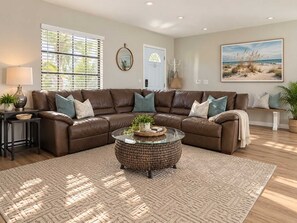 A living room with a brown leather sectional sofa, a glass coffee table, and a patterned rug.