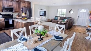 A modern kitchen with wooden cabinets, a central island, and a dining area with white chairs. - 798 Barefoot Bungalow ·Heated Pool/Spa· Bike2Beach (Naples)