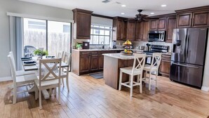 A modern kitchen with wooden cabinets, a central island, stainless steel appliances, and a dining area with white chairs. - 798 Barefoot Bungalow ·Heated Pool/Spa· Bike2Beach (Naples)