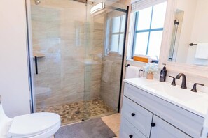 Une salle de bain moderne avec une douche à parois de verre, des toilettes blanches, un meuble-lavabo avec un miroir et un évier.