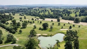 Un campo de golf con un estanque, rodeado de árboles y prados abiertos.