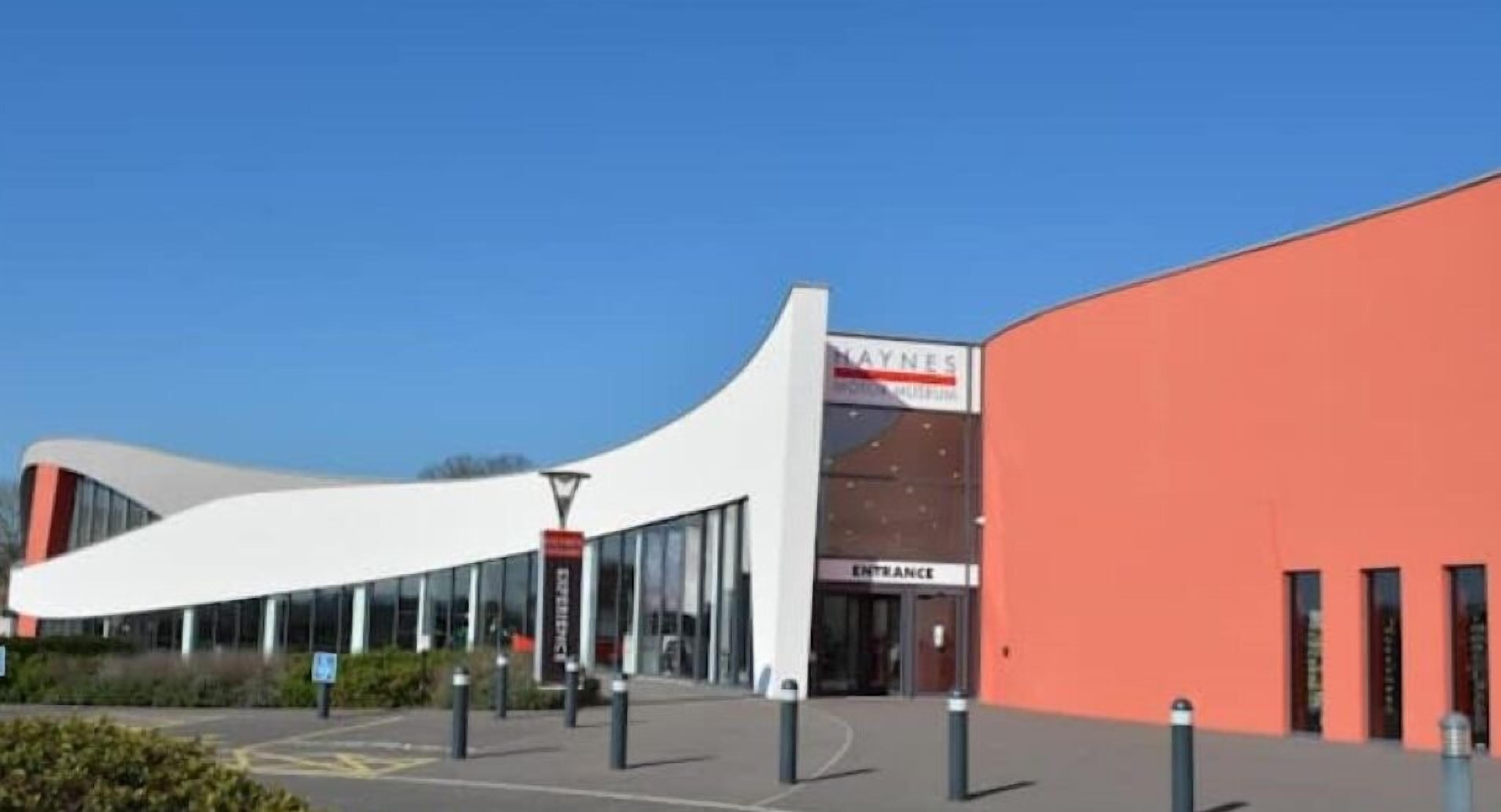 A modern building with a curved facade, a prominent entrance, and a sign for 'Maynes'.