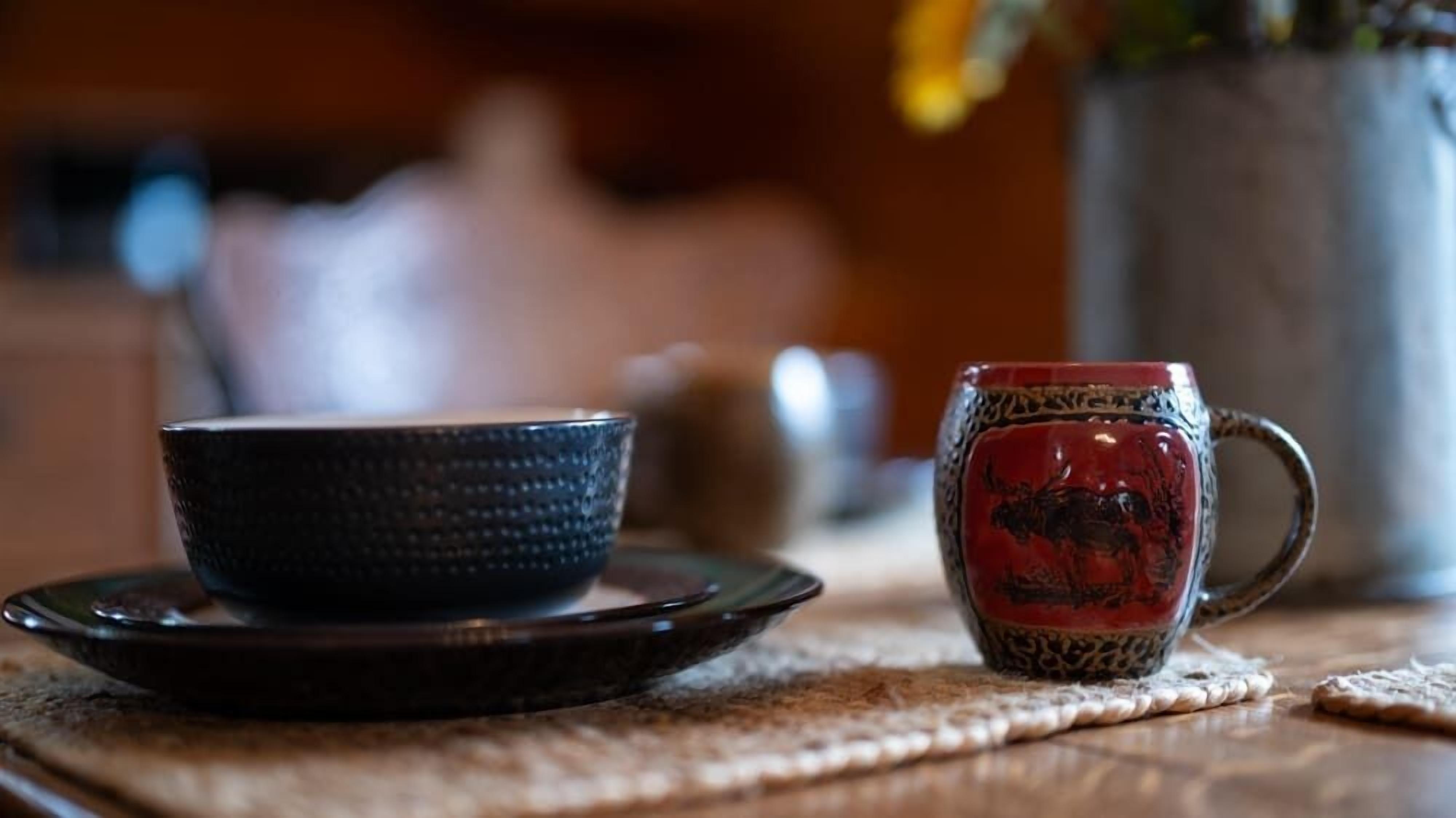 A table with a dark bowl and a red mug on a woven placemat.