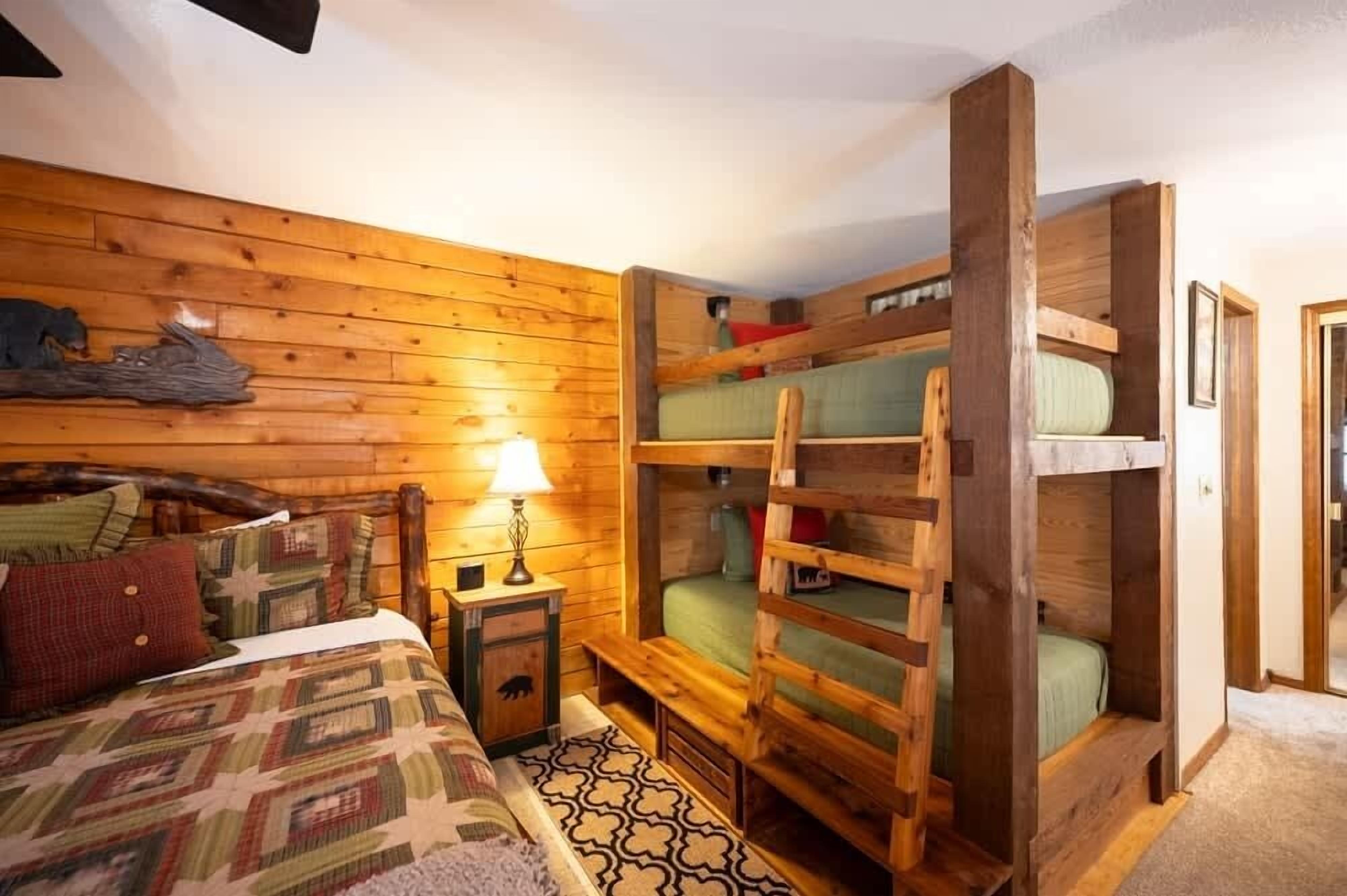 Une pièce confortable avec un lit superposé en bois, un lit simple avec une couvre-lit à motifs et une petite table de chevet avec une lampe.
