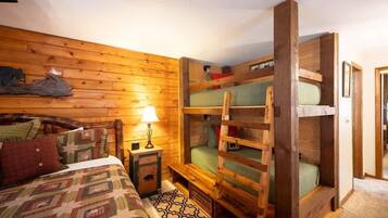 Une pièce confortable avec un lit superposé en bois, un lit simple avec une couvre-lit à motifs et une petite table de chevet avec une lampe.
