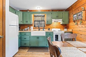A kitchen with green cabinets, a white refrigerator, a stove, and a dining table with chairs. - Log Cabin, Fire Pit, Hiking Trails, Porch Swing (Eureka Springs)