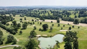 A golf course with a pond shaped like a heart, surrounded by trees and open grassy areas.