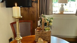 A dining table with a lit candle, bread, and a basket with bottles and flowers.