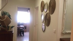 Un pasillo con piso de madera, una pared decorada con textiles trenzados y una puerta que da a un comedor.