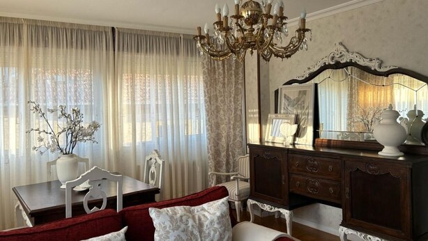 Una habitación con candelabro, espejo, cómoda, mesa con sillas y sofá.