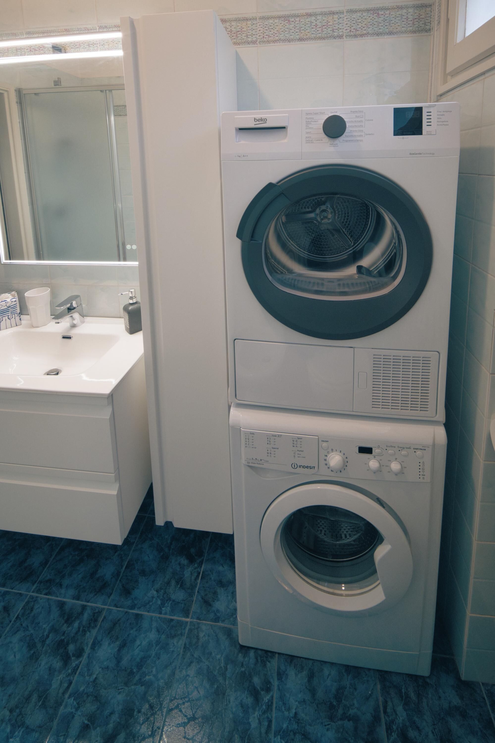 A stacked washer and dryer unit in a bathroom with a sink and mirror.