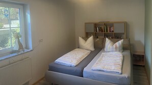 A small, well-lit room with two beds, a bookshelf, and a window. - 3 Zimmer Ferienwohnung, Schwarzwald, Nationalpark in der Nähe,haustierfreundlich (Baiersbronn)