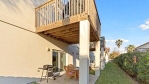 Ein Wohngebäude mit einer überdachten Terrasse, einem Grill und einer Sitzgruppe mit Stühlen.