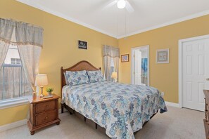Een slaapkamer met een bed, nachtkastjes, een dressoir, een plafondventilator en een deur.