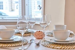 A table set with white bowls, wine glasses, and a decorative pink object, with a view of buildings through a window. - Modern Luxury 2-Bedroom Oasis in Heart of Whitley (Whitley Bay)
