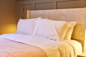 A neatly made bed with white linens and a textured blanket, a headboard with a light-colored panel, and a wall-mounted light fixture. - Modern Luxury 2-Bedroom Oasis in Heart of Whitley (Whitley Bay)