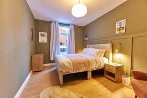 Ein Schlafzimmer mit Bett, Nachttisch, Lampe, Stuhl und einem kleinen Schrank.