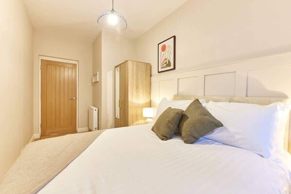 A bedroom with a bed, a wooden wardrobe, a door, and a wall-mounted picture. - Modern Luxury 2-Bedroom Oasis in Heart of Whitley (Whitley Bay)