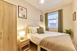 Een hotelkamer met een bed, nachtkastje, lamp, gordijnen en kunst aan de muren.