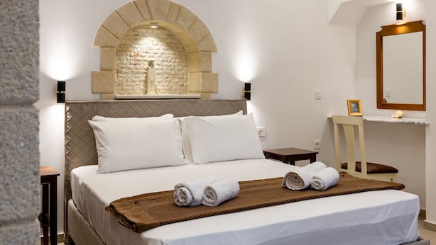 A hotel room with a large bed, a stone arch wall, a wooden chair, and a bedside table. - The Owl House (Chania)