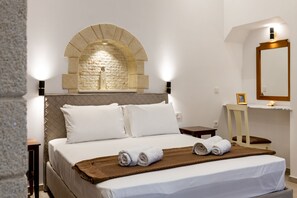 A hotel room with a large bed, a stone arch wall, a wooden chair, and a bedside table. - The Owl House (Chania)